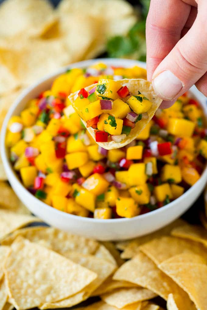 A hand holding a tortilla chip topped with mango salsa.