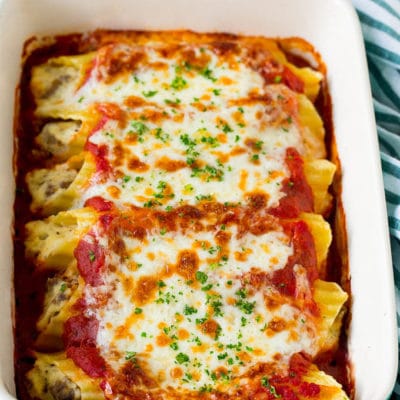 A dish of baked manicotti pasta topped with melted cheese and parsley.
