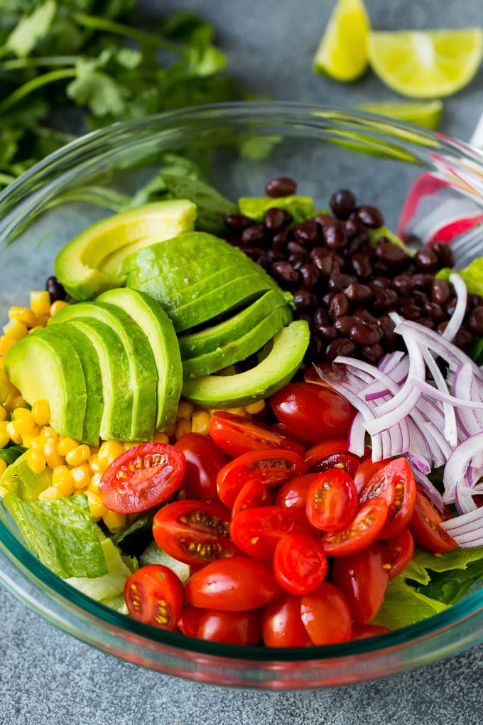 Lettuce, tomatoes, onion, corn, avocado and black beans in a bowl.