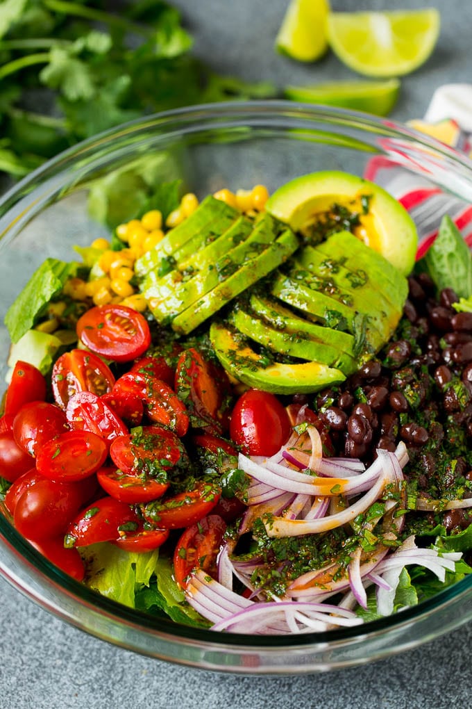 Dressing poured over a bowl of lettuce, tomatoes, avocado and beans.