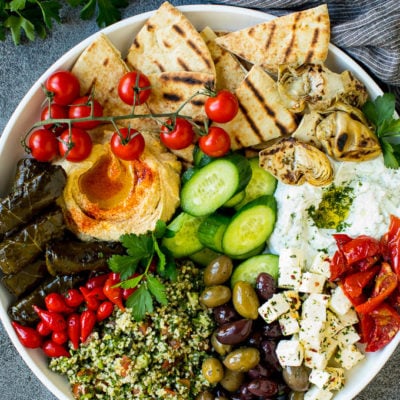 A mezze platter filled with dips, pita bread, vegetables, olives and cheese.