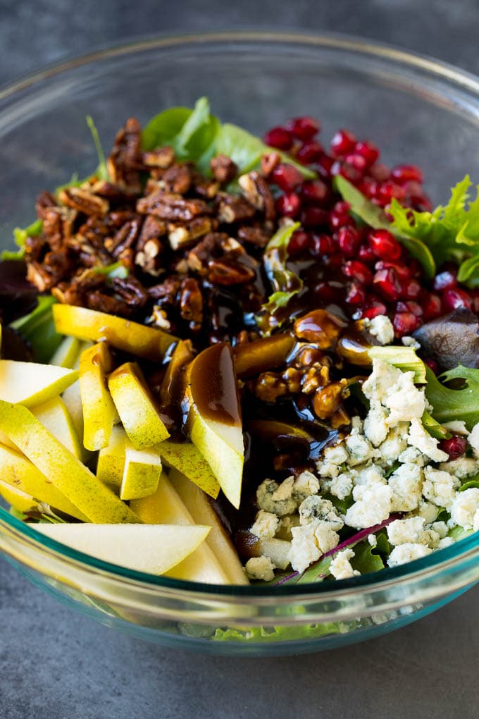 Balsamic dressing poured over a bowl of mixed greens, sliced pears and pomegranate seeds.