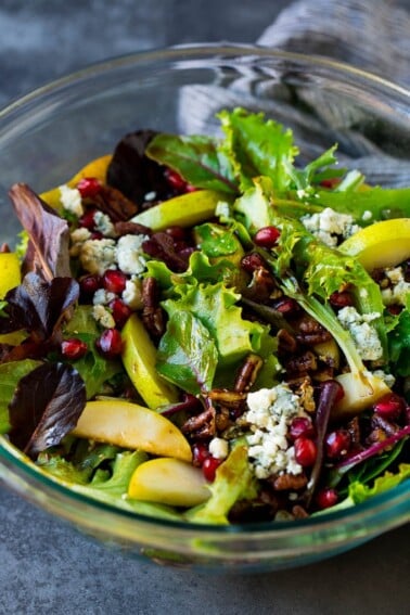 A bowl of pear salad with pomegranate, blue cheese and candied pecans.