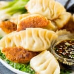 A plate of potstickers served with dipping sauce.