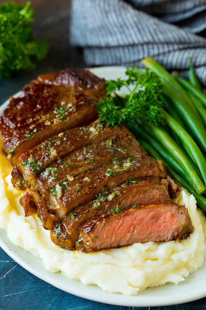 Sliced sirloin steak over mashed potatoes with green beans.