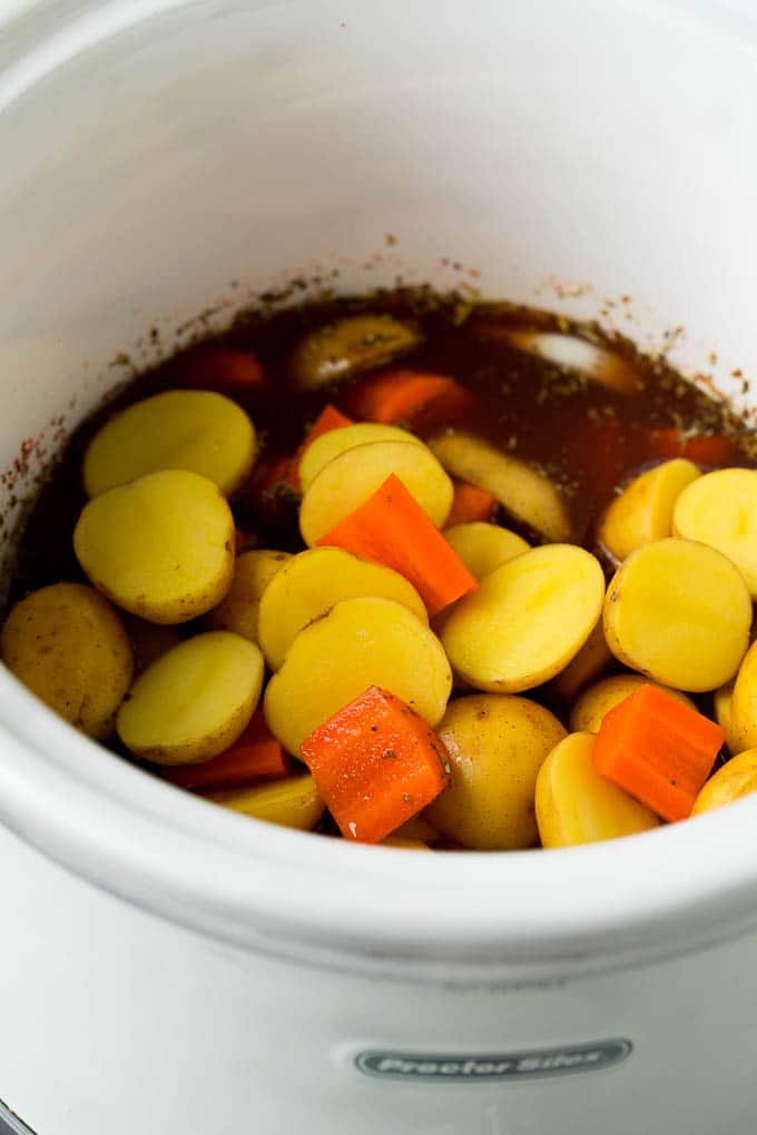 Potatoes, carrots and seasonings in a crockpot.