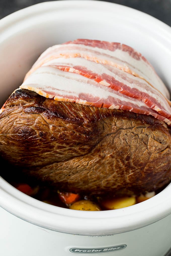 Bacon wrapped beef roast in a slow cooker.
