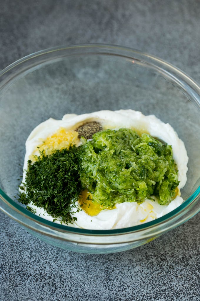 A bowl of yogurt with shredded cucumber, fresh dill and garlic.