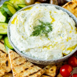 A bowl of tzatziki served with pita bread and vegetables.