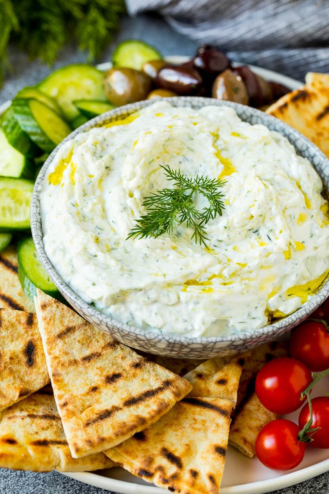 A bowl of tzatziki served with pita bread and vegetables.