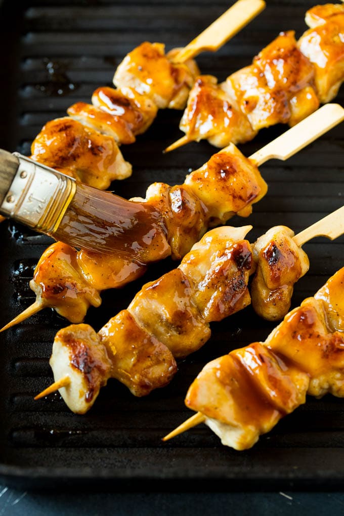 A basting brush putting sauce onto grilled chicken yakitori..