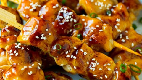 A plate of grilled chicken yakitori topped with sesame seeds and green onions.