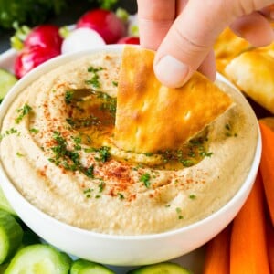 A hand dipping pita bread into baba ganoush.