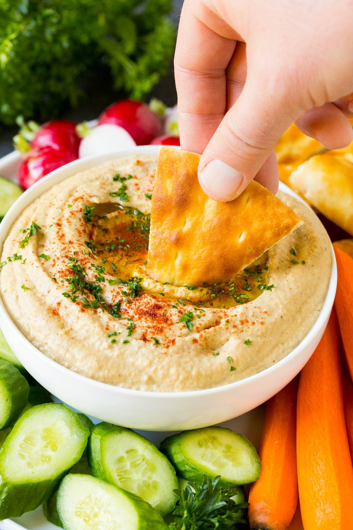 A hand dipping pita bread into baba ganoush.