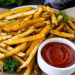 A plate of baked french fries served with ketchup.
