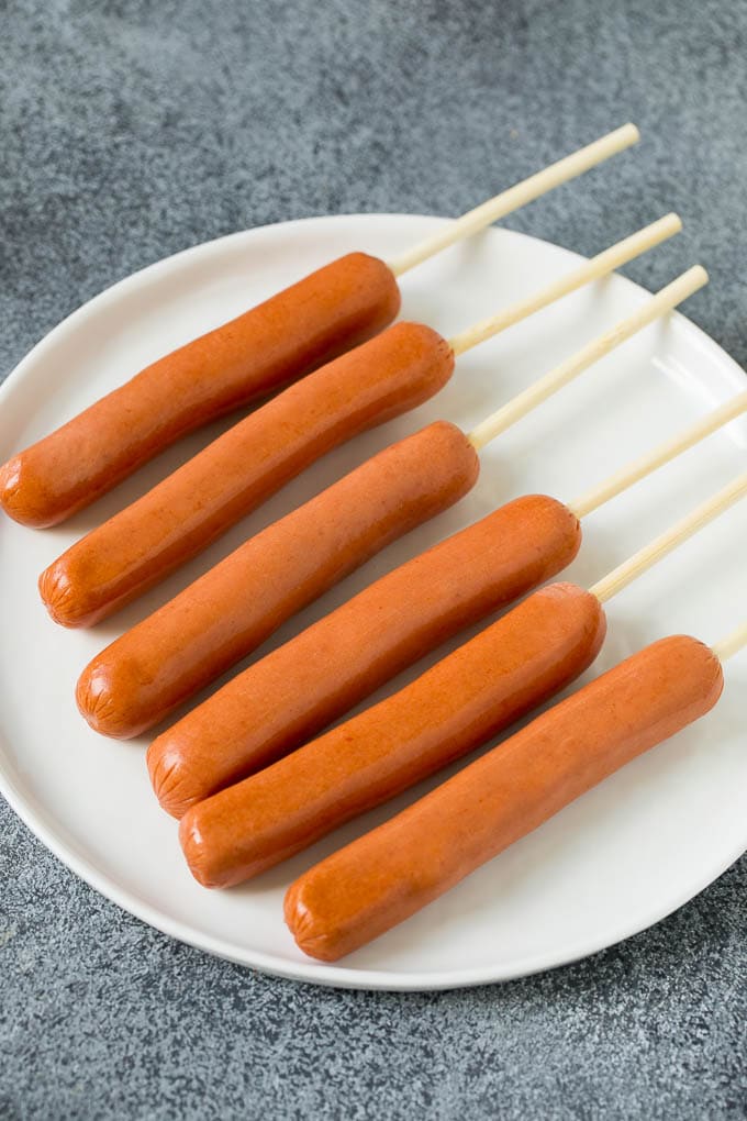 Hot dogs on sticks on a plate.