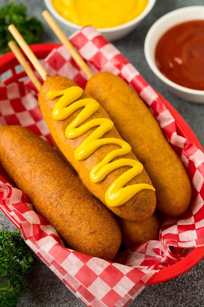 A basket of corn dogs with one topped with mustard.