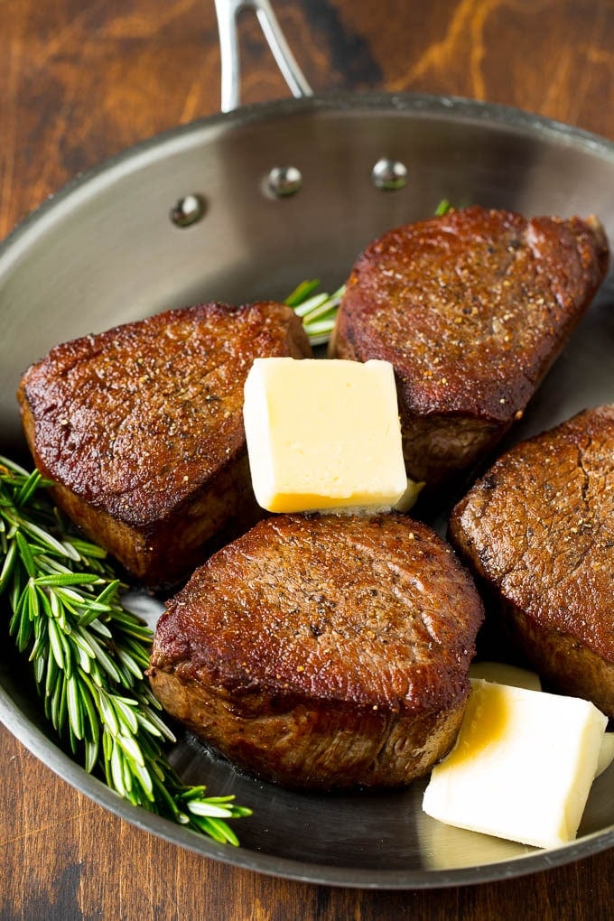 Cooked steaks with pats of butter, rosemary and garlic.