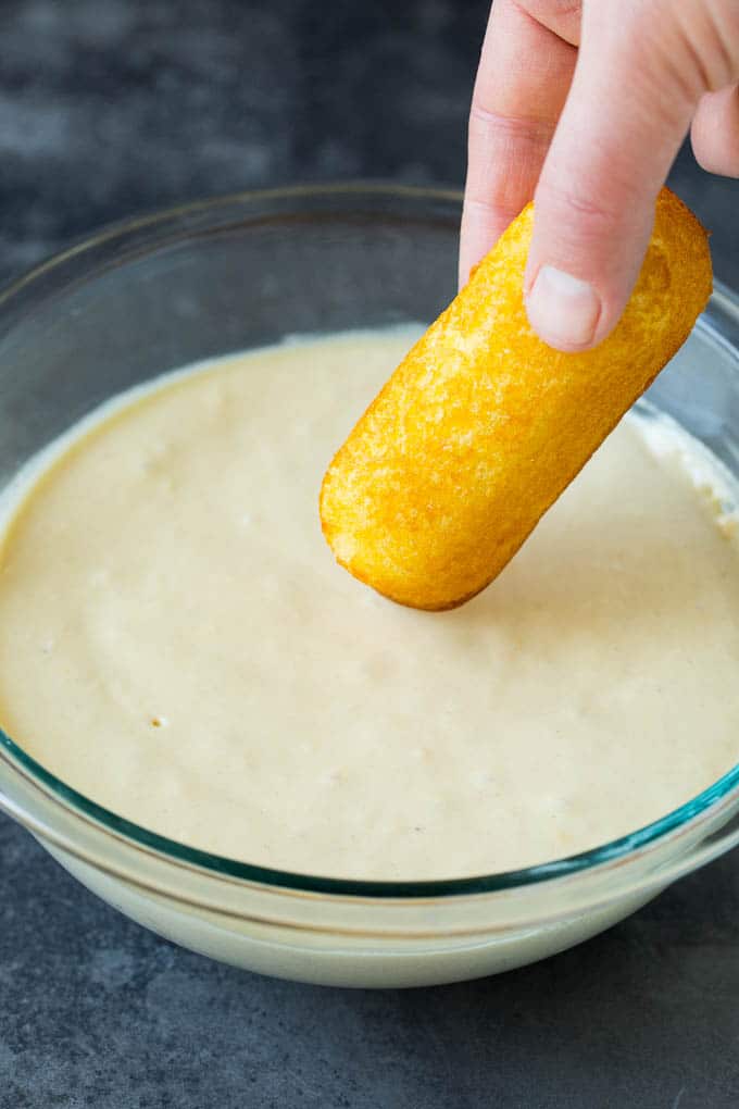 A Twinkie being dipped into a bowl of batter.