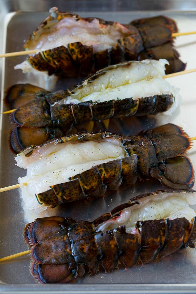 Raw lobster tails split open with skewers through them.