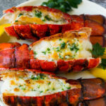 Grilled lobster tail topped with garlic butter and garnished with lemon and parsley.