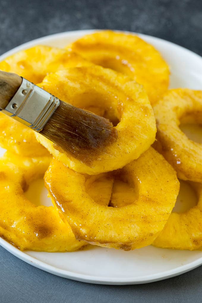 A brush coating pineapple slices with butter and brown sugar.