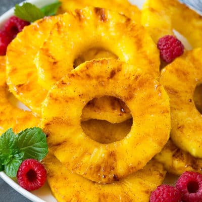 A plate of grilled pineapple slices garnished with raspberries and mint.