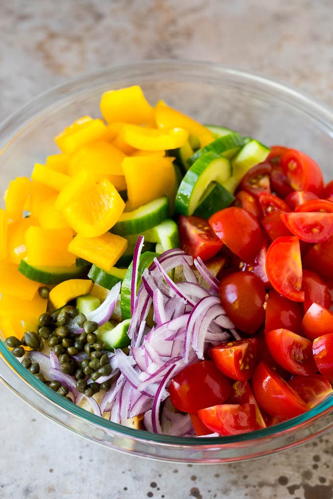 Tomatoes, bell peppers, cucumbers, red onion and capers in a bowl.