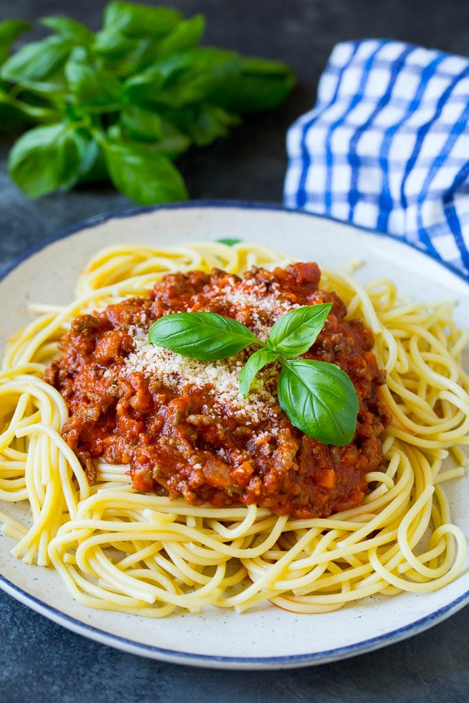 A plate of pasta bolognese topped with parmesan cheese and fresh basil.