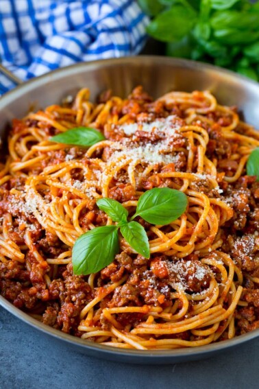 A pan of pasta bolognese garnished with basil sprigs and parmesan cheese.