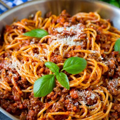 A pan of pasta bolognese garnished with basil sprigs and parmesan cheese.