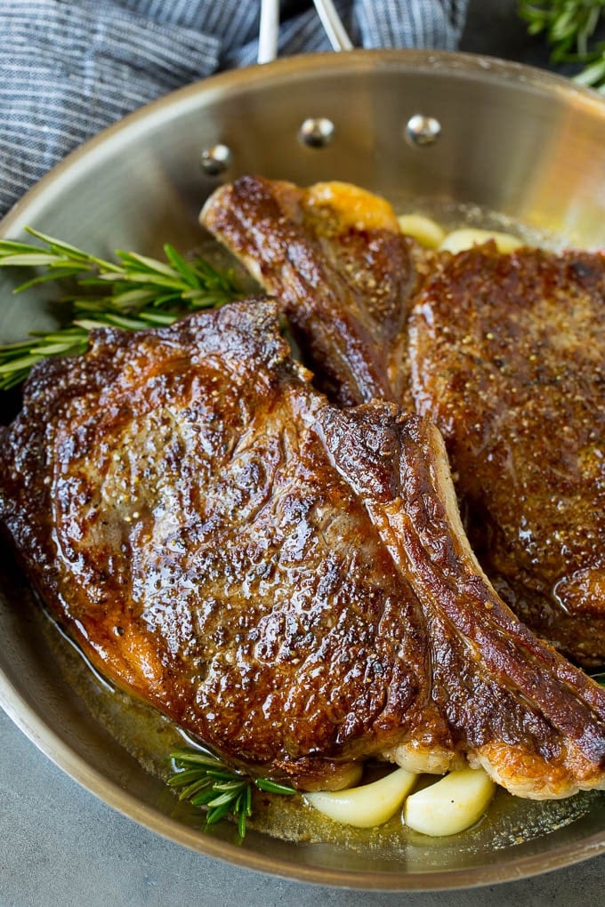 Rib eye steak with garlic butter and rosemary in a skillet.