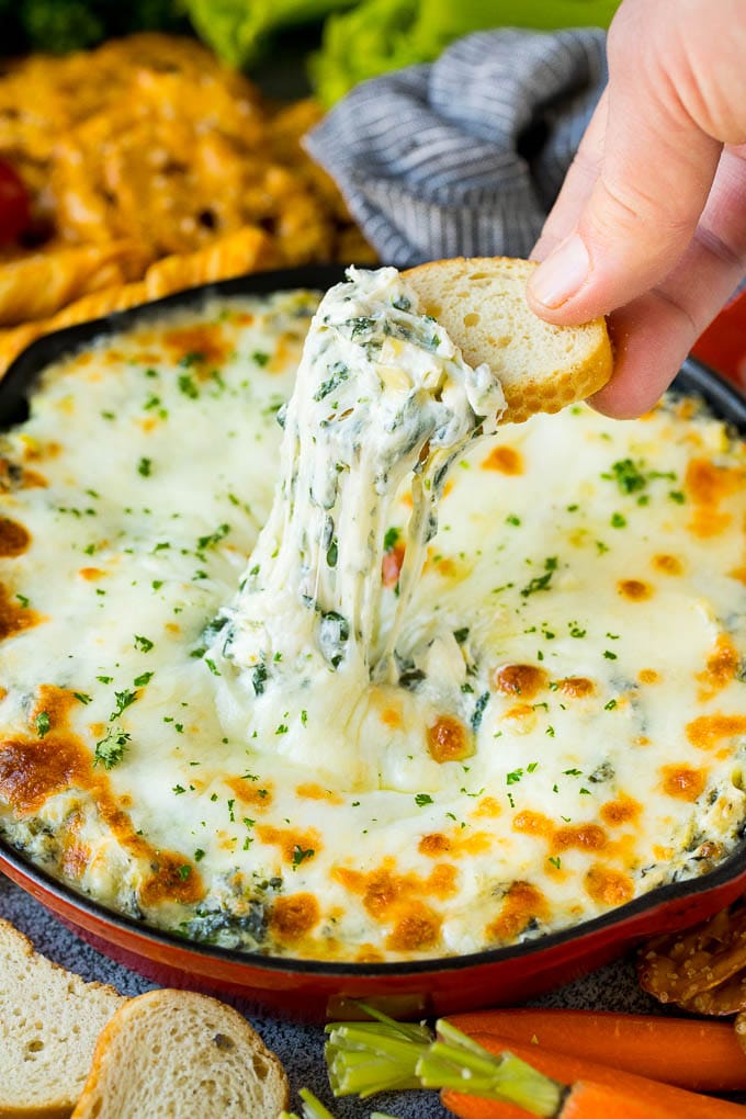 A hand scooping out a portion of spinach artichoke dip.