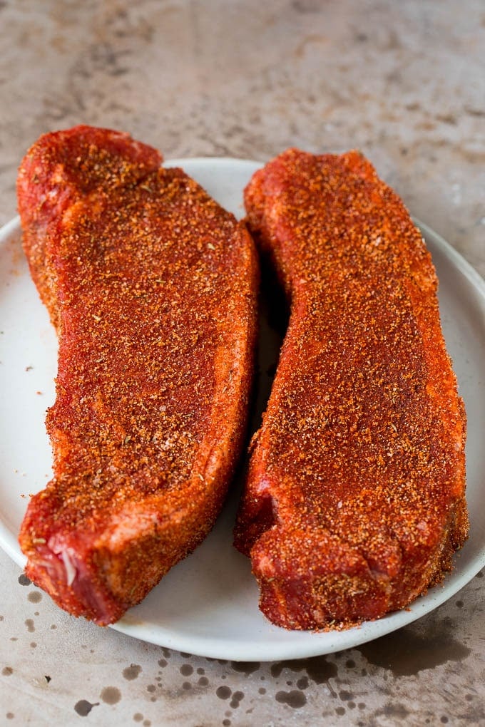 Steaks coated in seasoning on a plate.