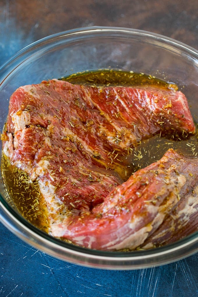 A piece of tri tip steak in a bowl of marinade.