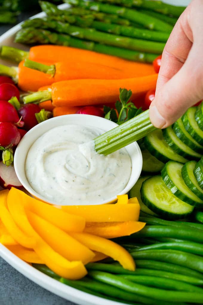 A hand dipping celery into ranch sauce.