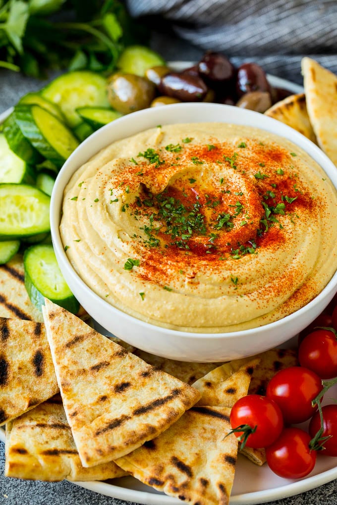 A bowl of homemade hummus with pita bread and vegetables.