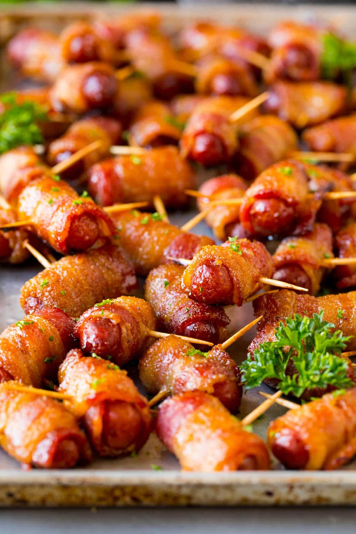A sheet pan full of bacon wrapped smokies, garnished with parsley.