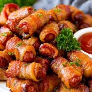 A serving plate of bacon wrapped smokies with parsley and a side of ketchup.