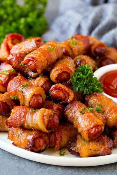 A serving plate of bacon wrapped smokies with parsley and a side of ketchup.