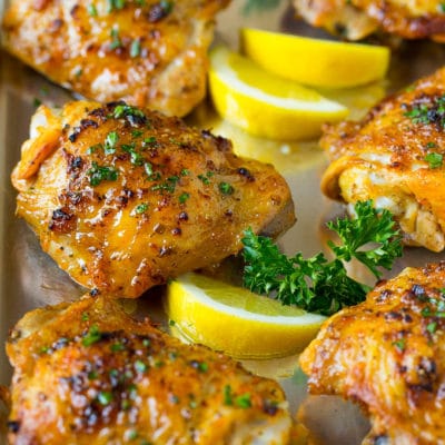 A pan of baked chicken thighs garnished with parsley and lemon.