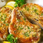 Baked pork chops in garlic butter, garnished with parsley and lemon.