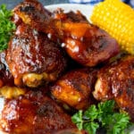 A platter of BBQ chicken garnished with corn on the cob and parsley.