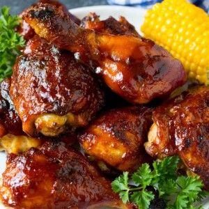 A platter of BBQ chicken garnished with corn on the cob and parsley.