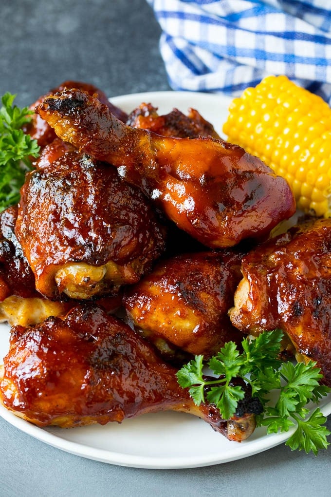 A platter of BBQ chicken garnished with corn on the cob and parsley.
