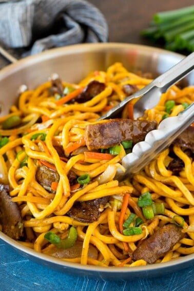 Tongs serving up a portion of beef lo mein.