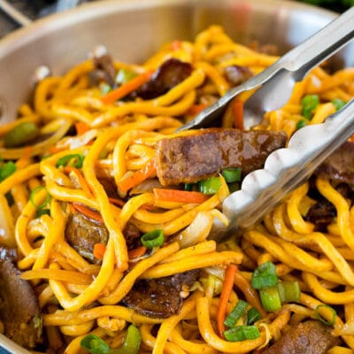 Tongs serving up a portion of beef lo mein.