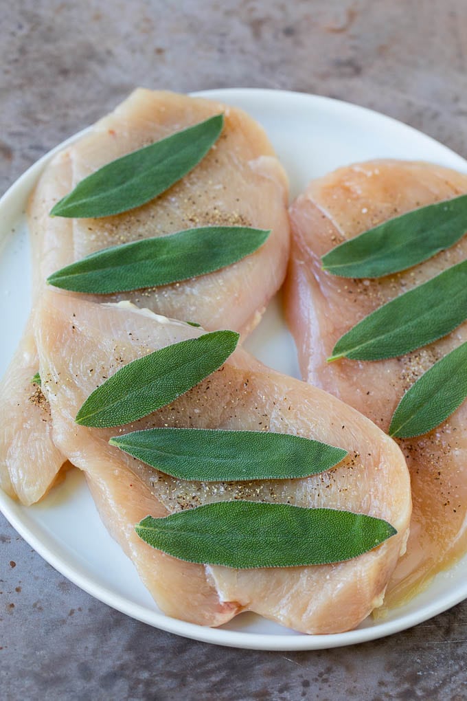 Chicken breasts with fresh sage leaves on top.