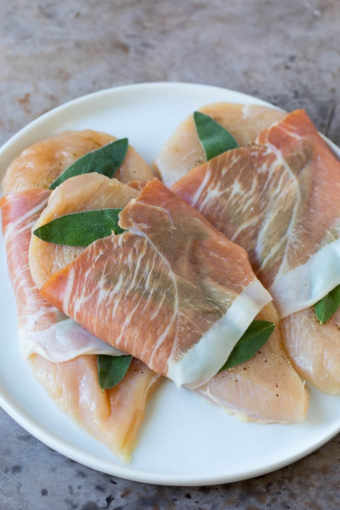 Raw chicken topped with fresh sage leaves and prosciutto.