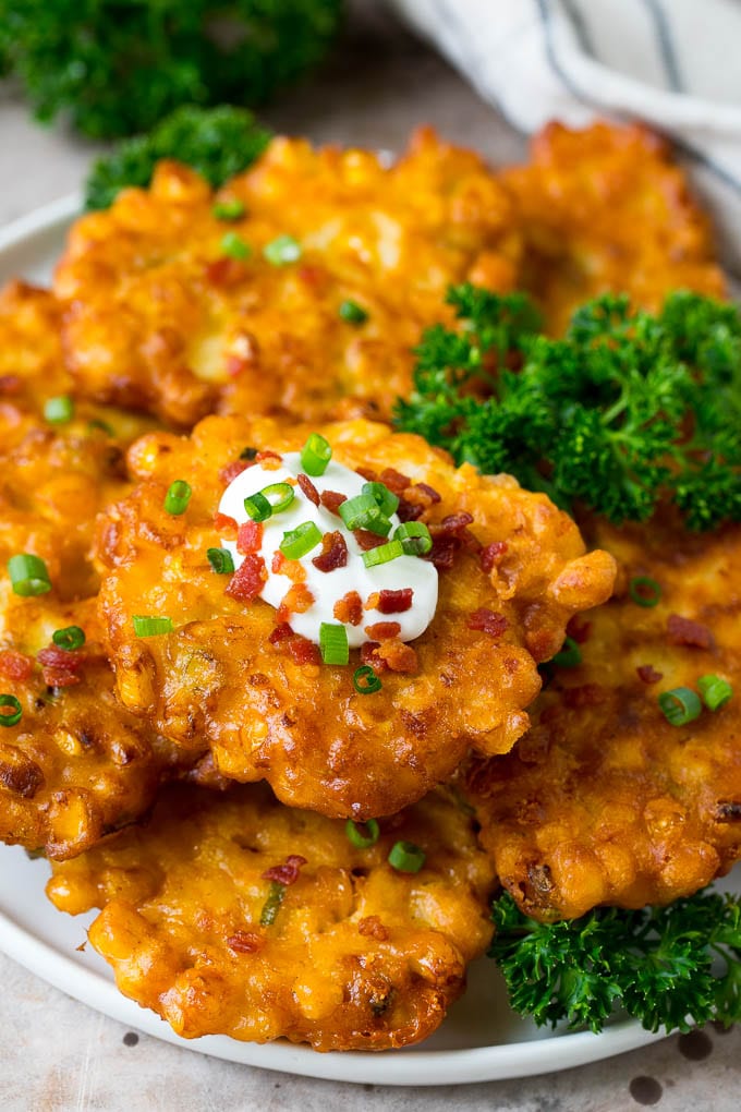 A plate of corn fritters garnished with parsley, and topped with sour cream.